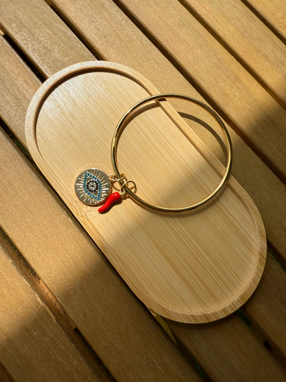 Bracelet jonc doré Chiara avec deux breloques décoratives présenté sur une surface en bois
