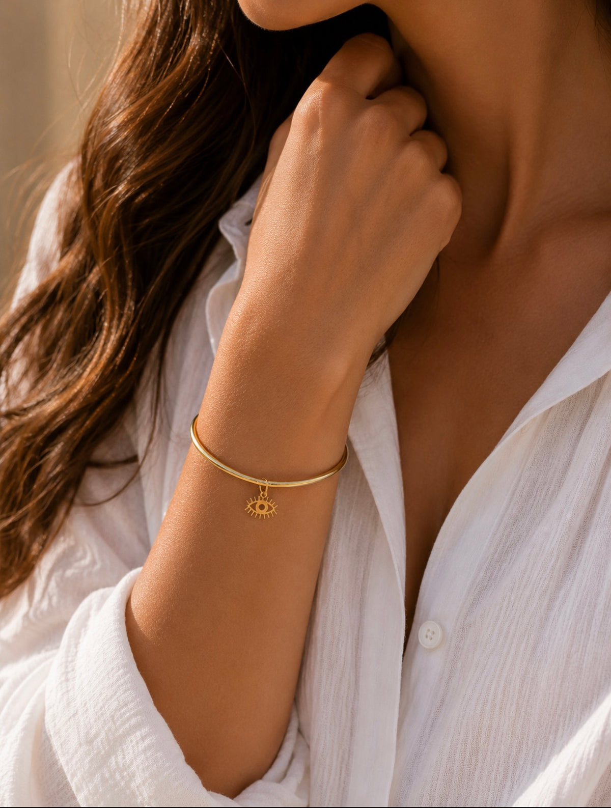 Bracelet jonc Romane doré en acier inoxydable porté au poignet d'une femme en chemise blanche