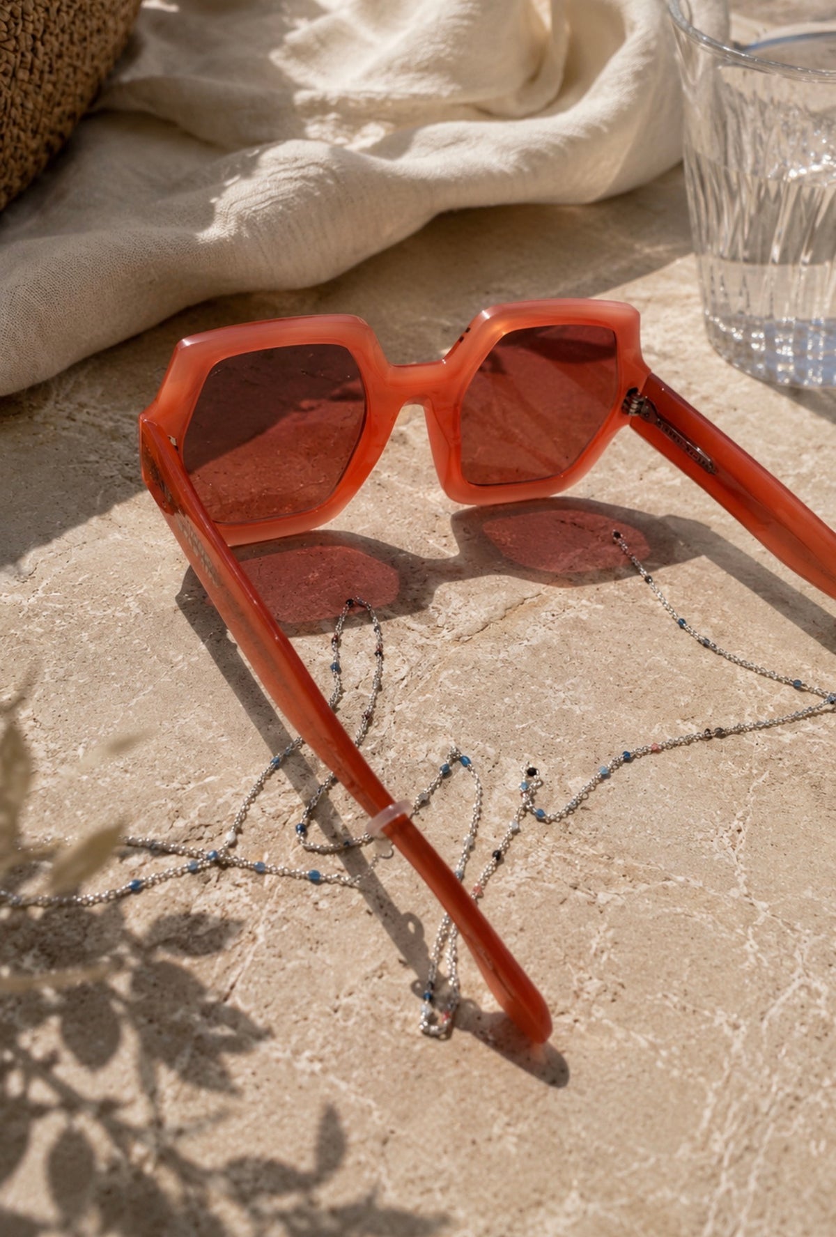 Lunettes de soleil orange avec chaîne de lunettes Madeline argentée, présentées sur une surface claire