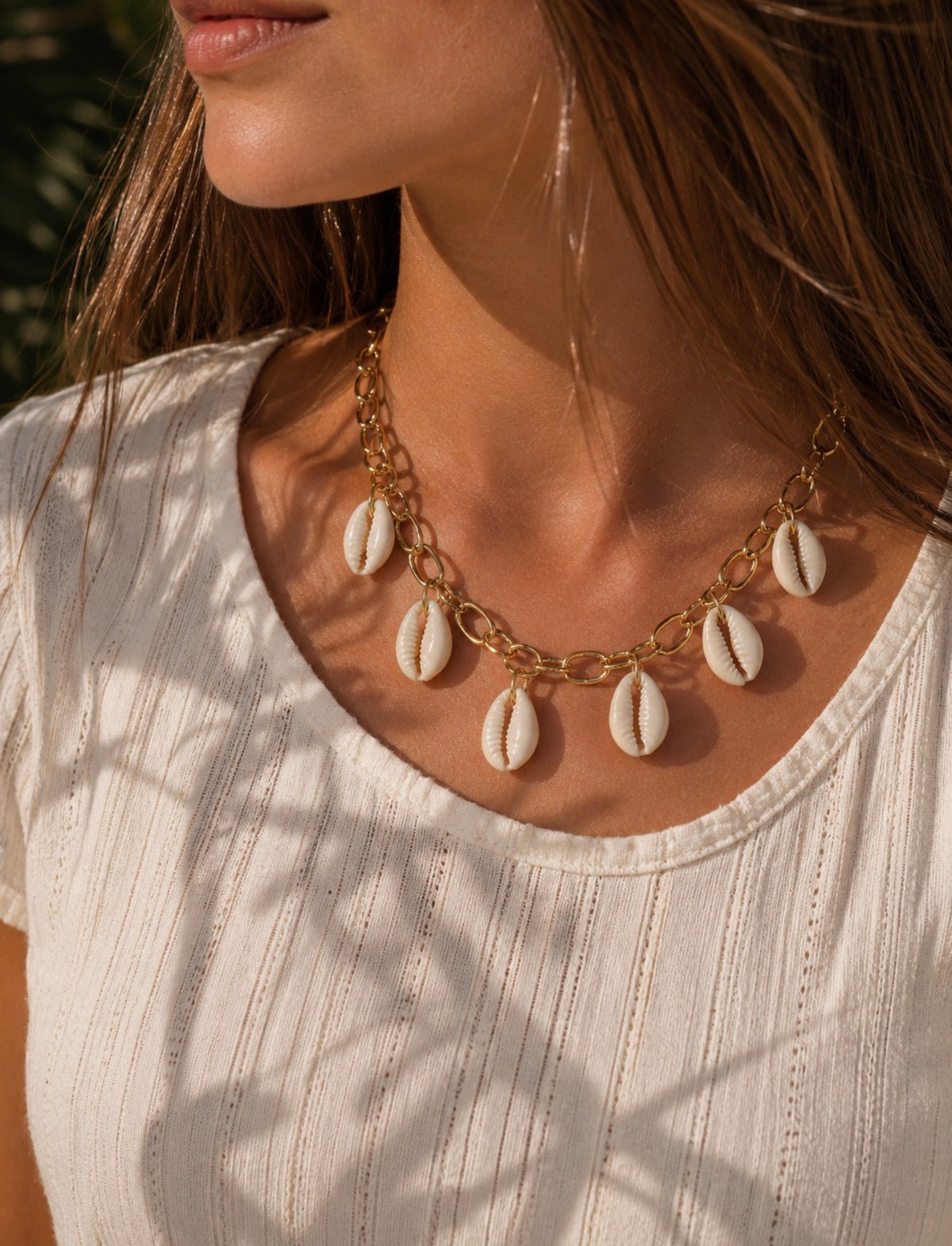 Collier Kiara doré avec plusieurs coquillages blancs, porté par une femme en haut blanc