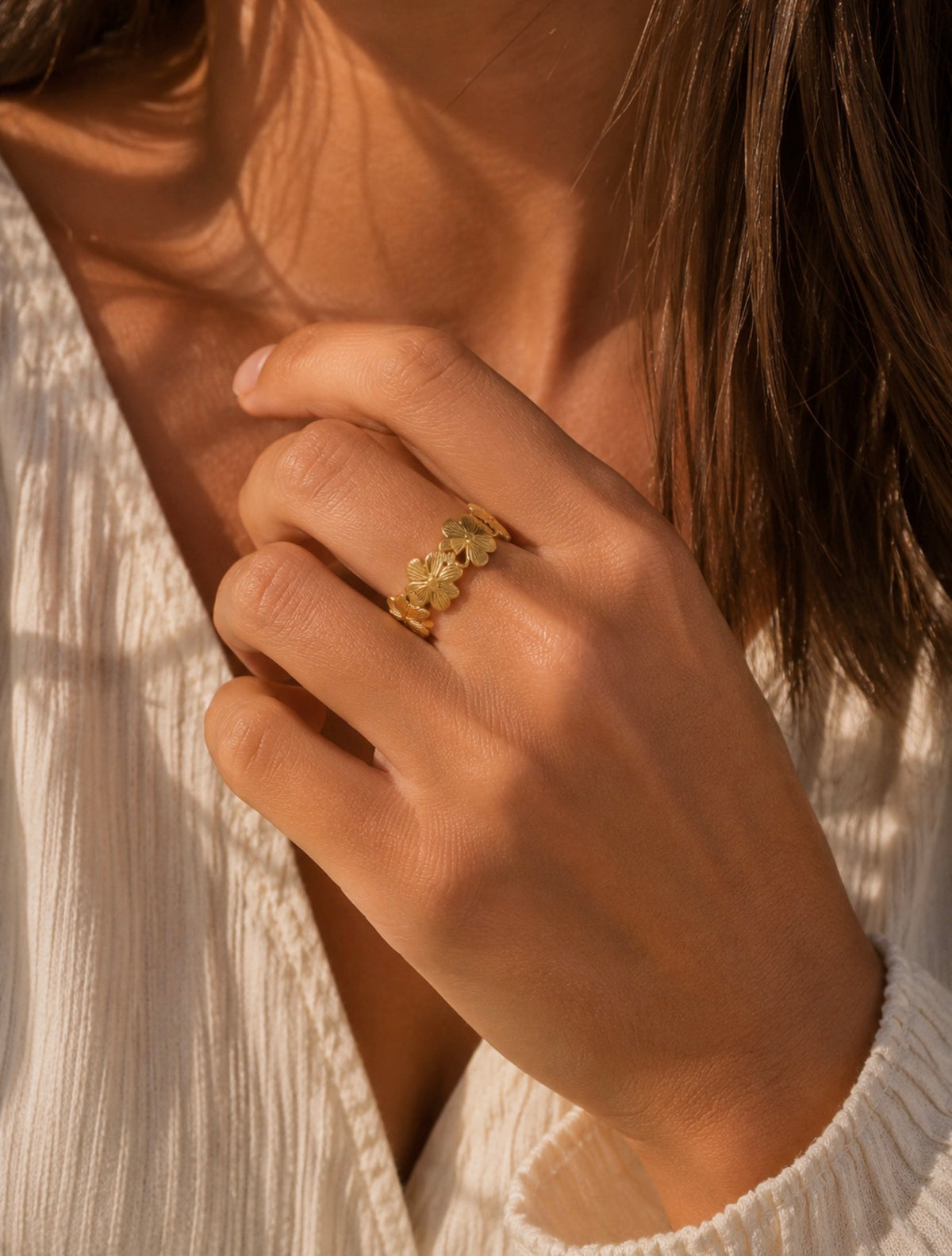 Bague Millie en acier inoxydable doré avec motif fleur, portée au doigt d'une femme en chemise blanche
