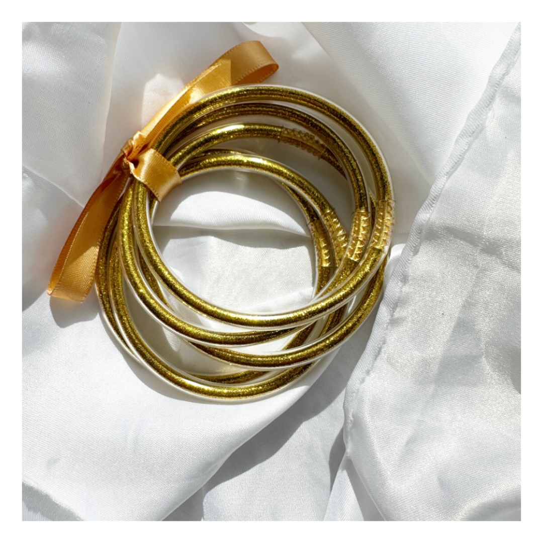 Ensemble de bracelets joncs bouddhistes Lucie dorés disposés en cercle sur un tissu blanc