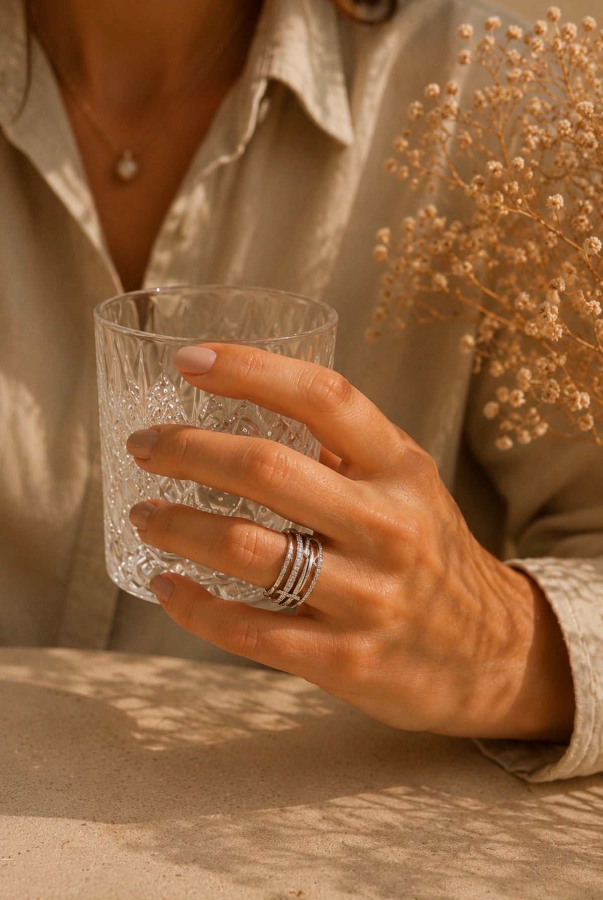 Bague Sienna large argentée en acier inoxydable portée à la main d'une femme tenant un verre