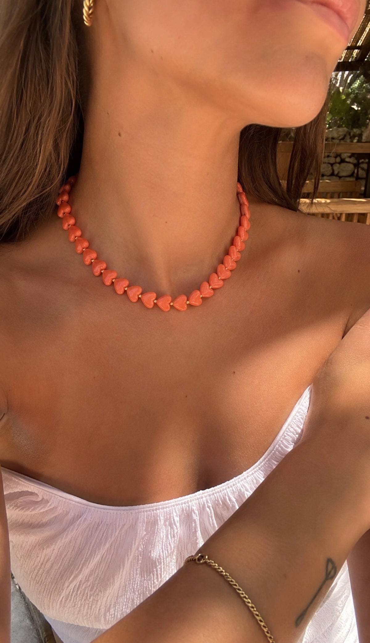 Collier Ama orange corail composé de perles en forme de cœur, porté par une femme avec un haut blanc. Bijou fantaisie coloré et tendance LAU.THENTIK.