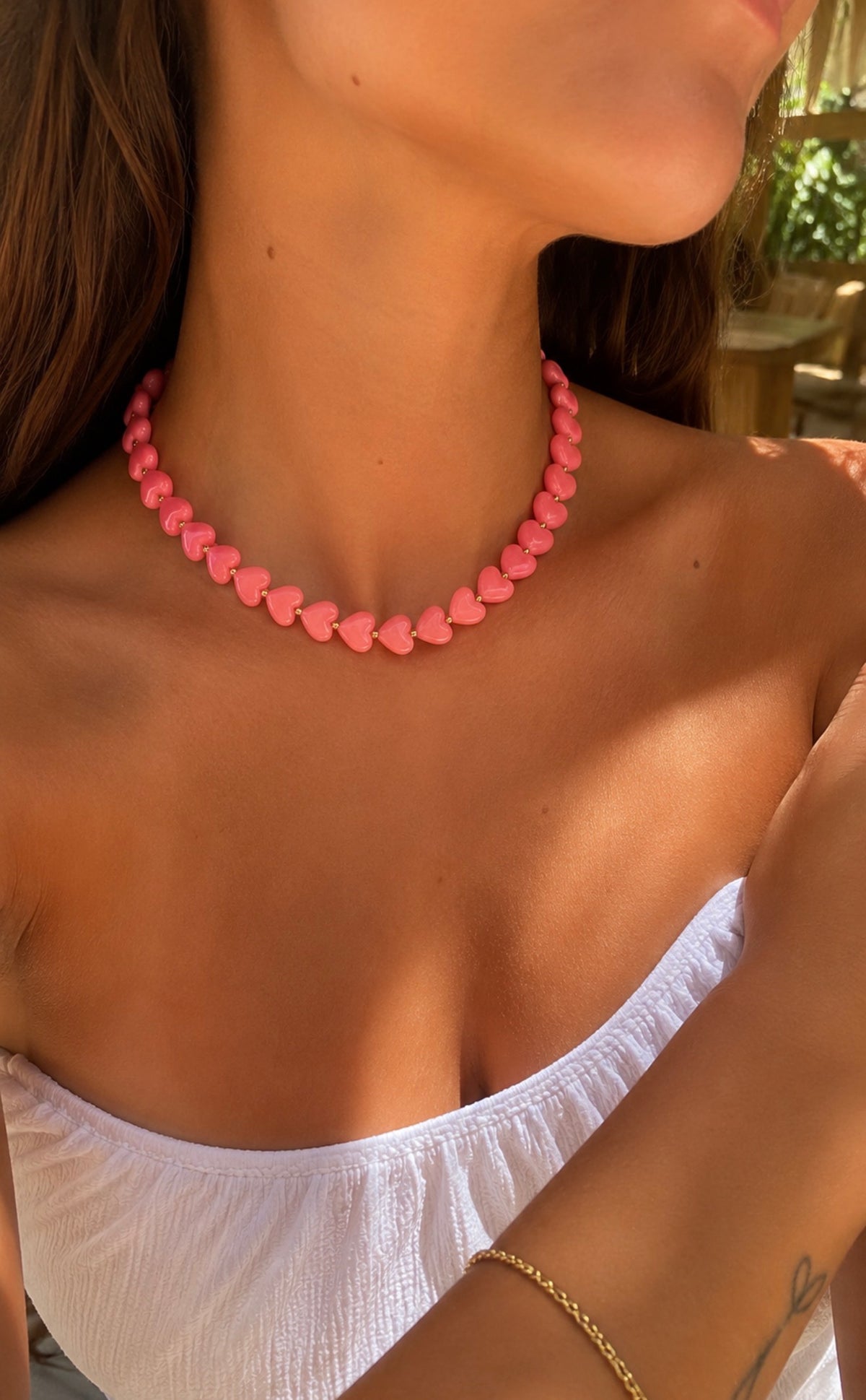 Collier Ama rose corail composé de perles en forme de cœur, porté par une femme avec un haut blanc. Bijou fantaisie coloré LAU.THENTIK.