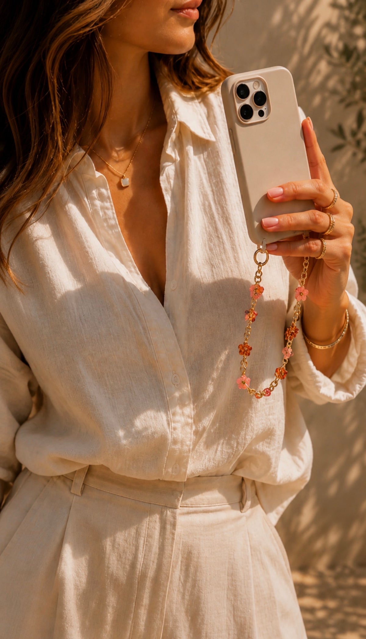 Bijou de téléphone Inès doré accroché à une coque de smartphone blanc, tenu par une femme en chemise blanche