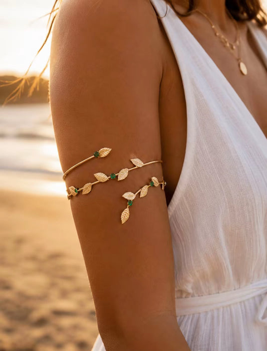 Bijou de bras Tiphaine doré avec petites feuilles vertes porté sur le haut du bras d'une femme en robe blanche