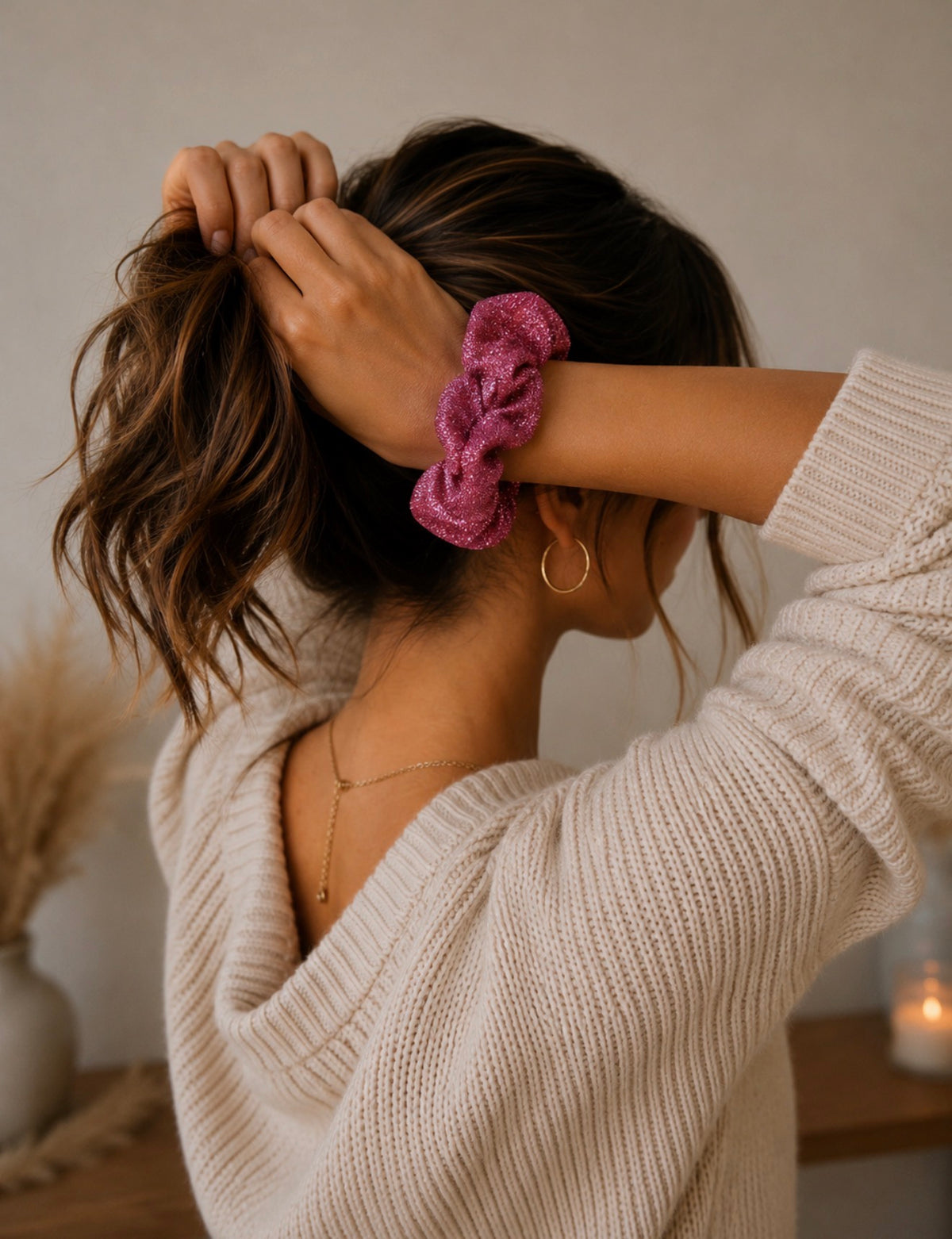 Chouchou rose à paillettes porté au poignet d'une femme aux cheveux attachés, avec un pull blanc