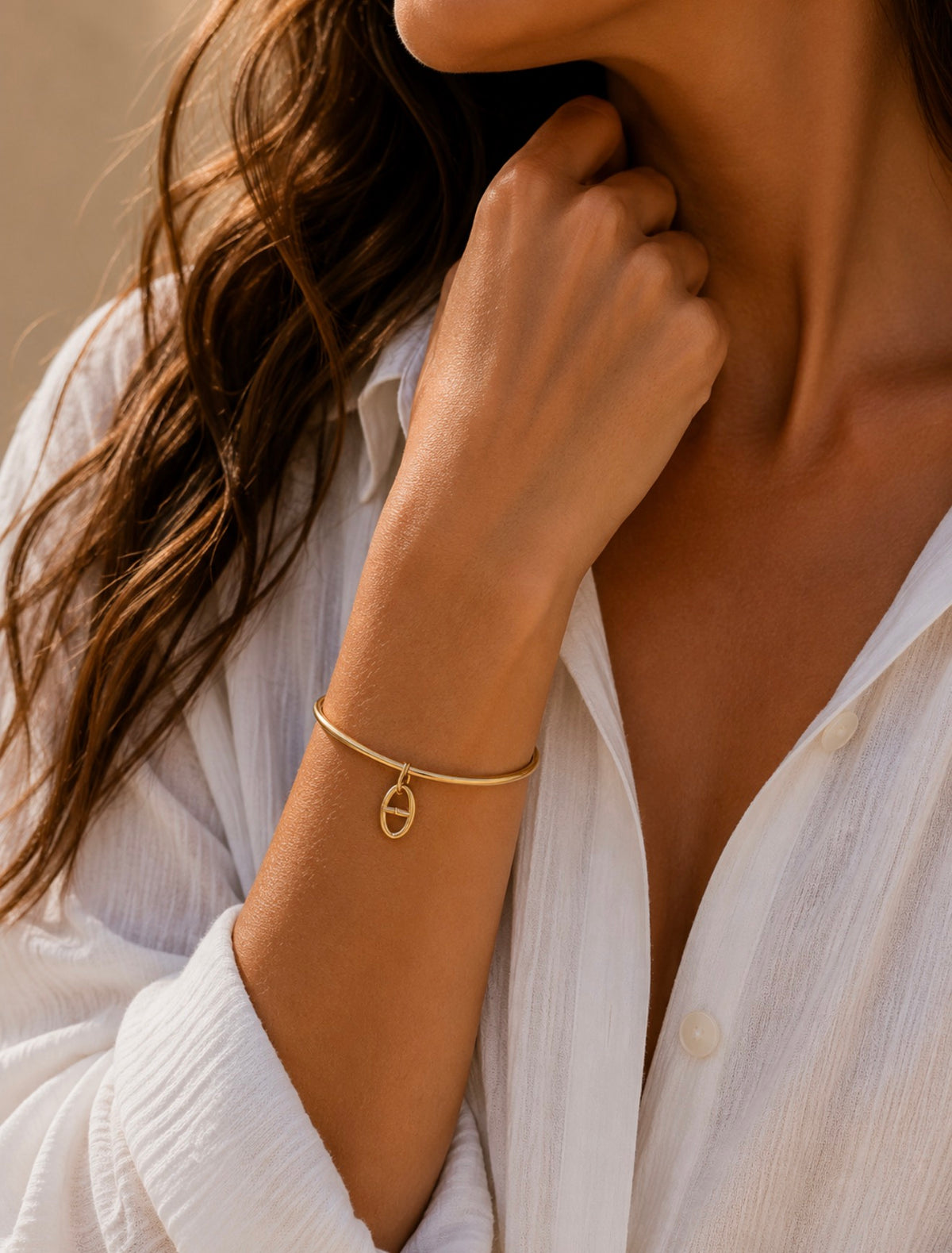 Bracelet jonc Adèle doré avec petite breloque maille marine, porté au poignet d'une femme en chemise blanche