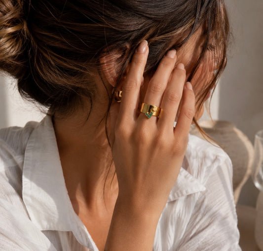Bague Liza dorée avec petite breloque verte portée au doigt d'une femme en chemise blanche