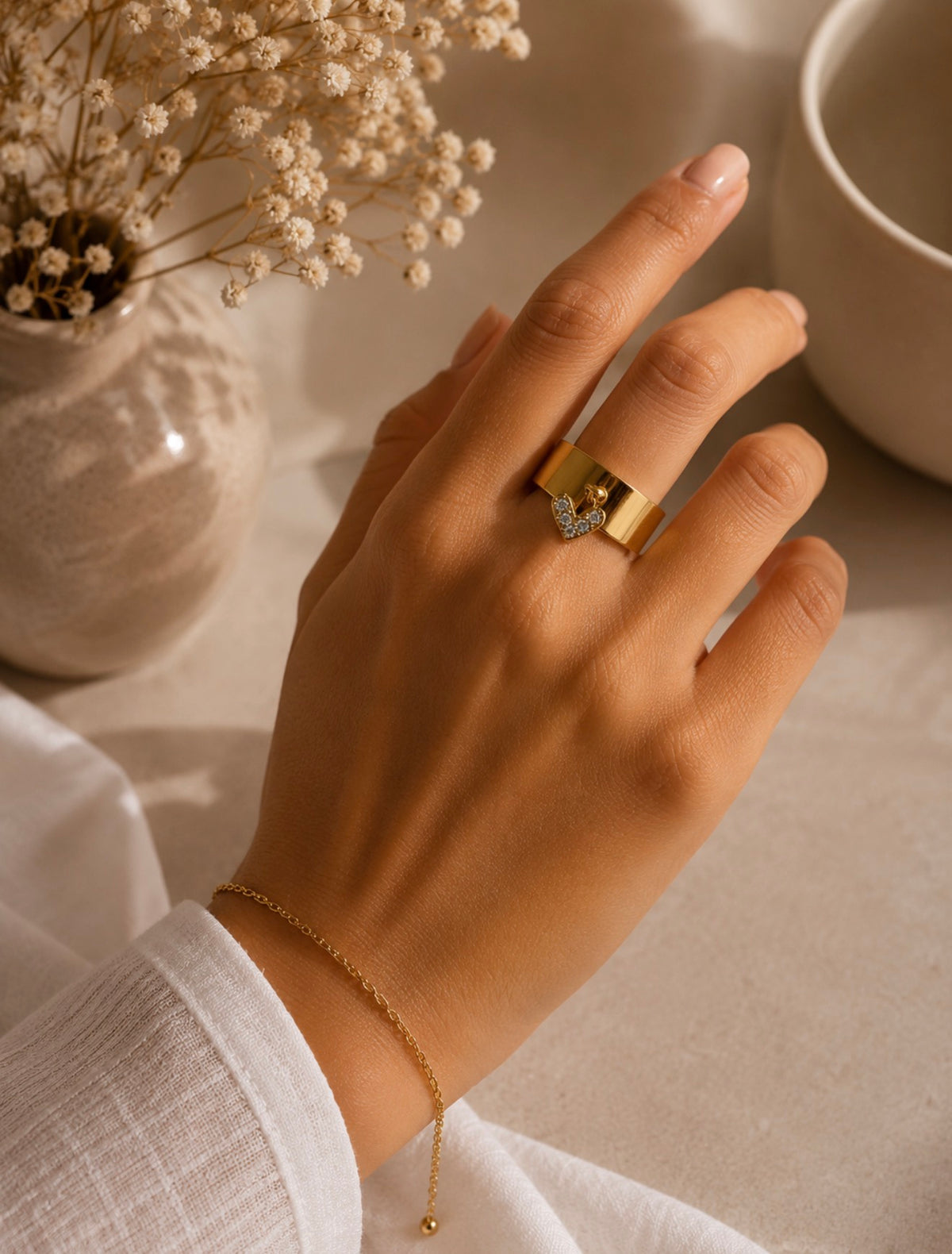 Bague Flora dorée avec détail décoratif portée au doigt d'une femme près d'une tasse blanche