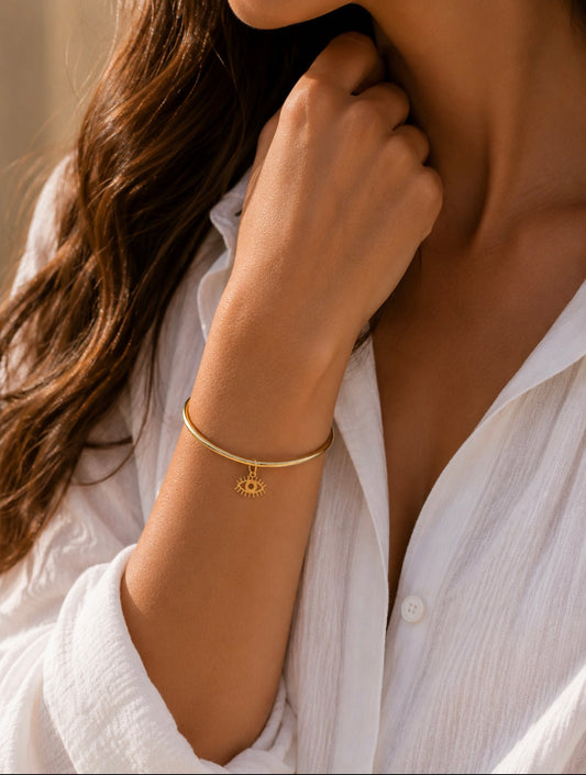 Bracelet jonc Romane doré en acier inoxydable porté au poignet d'une femme en chemise blanche