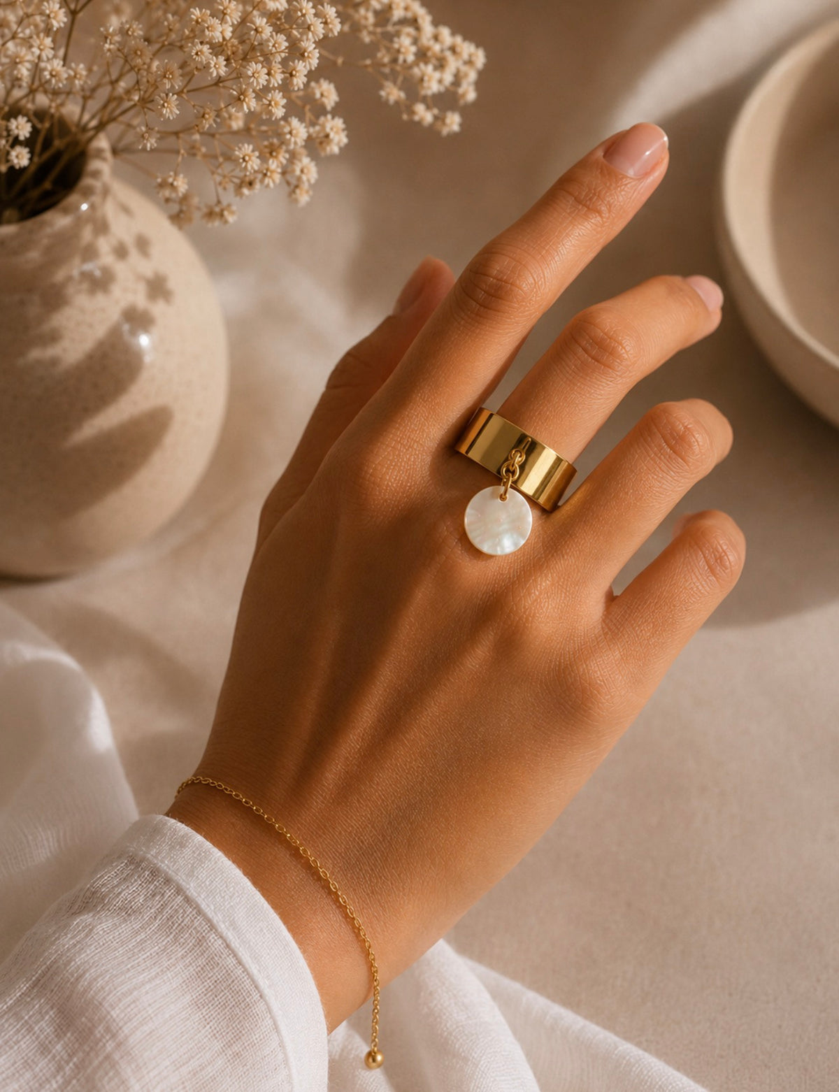 Bague Melina dorée à anneau large avec breloque blanche nacrée, portée au doigt d'une femme