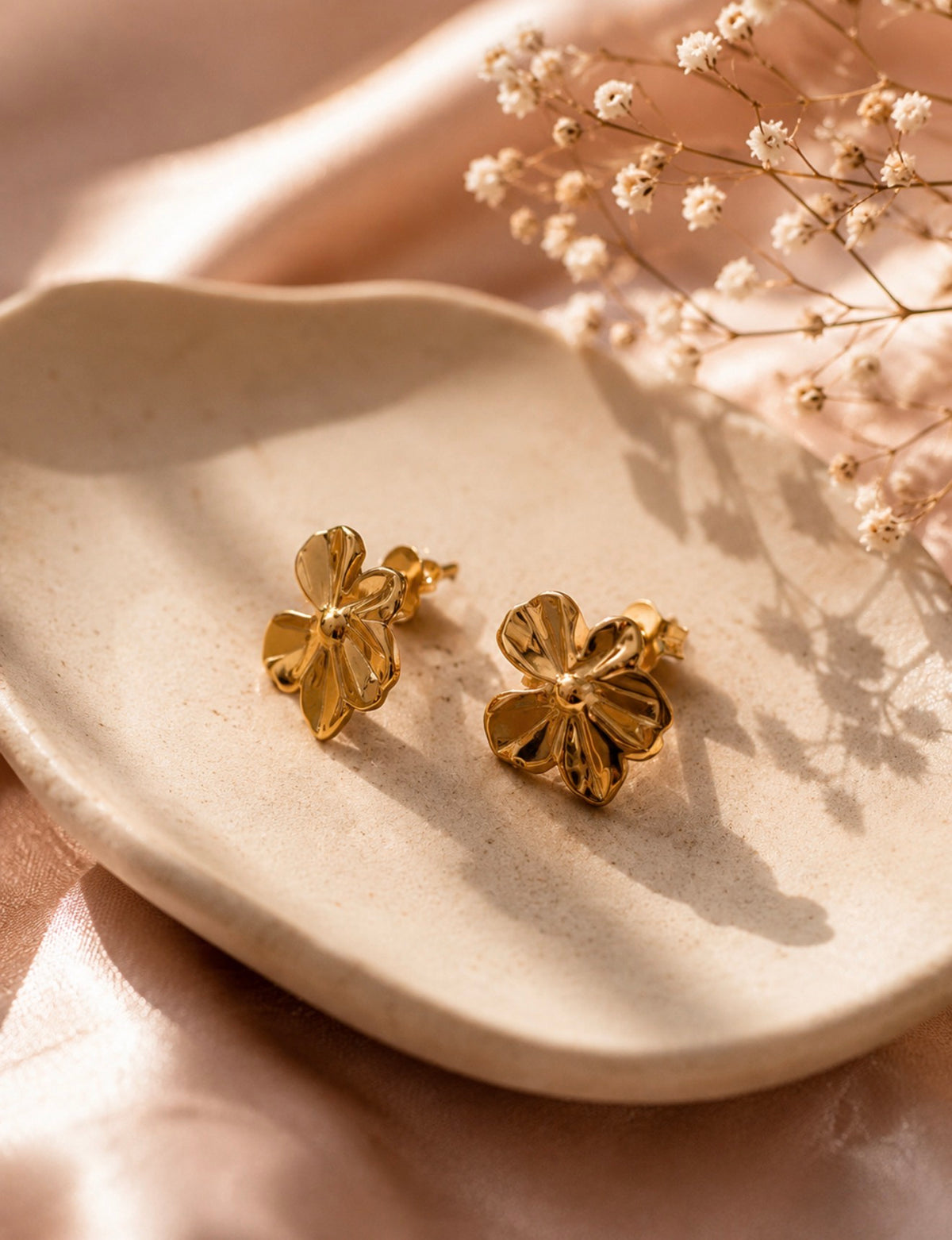 Paire de boucles d'oreilles Melissa en forme de fleurs dorées présentée sur un petit plateau blanc