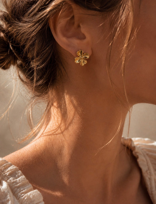 Boucle d'oreille Melissa dorée en forme de fleur portée à l'oreille d'une femme