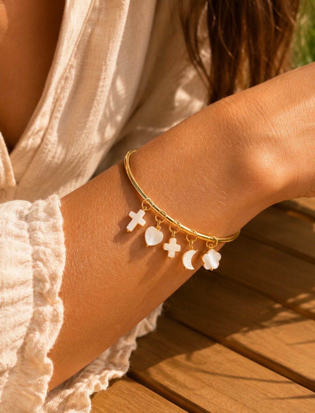 Bracelet jonc doré avec plusieurs breloques blanches suspendues, porté au poignet d'une femme
