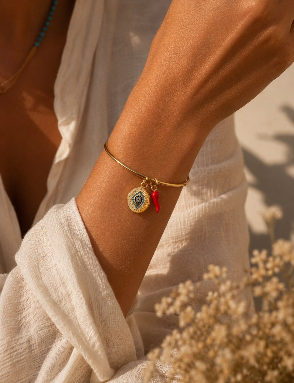 Bracelet jonc Chiara doré avec deux breloques colorées porté au poignet d'une femme