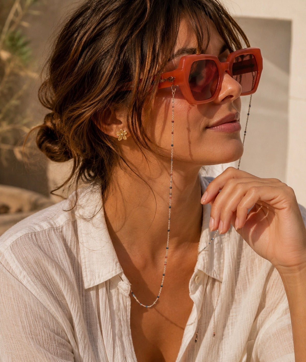 Chaîne de lunettes Madeline argentée portée par une femme avec des lunettes de soleil orange et une chemise blanche