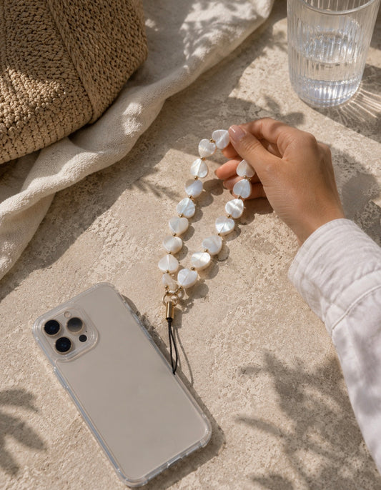 Bijou de téléphone Emmy avec perles blanches et détails dorés, tenu à la main à côté d'un smartphone blanc