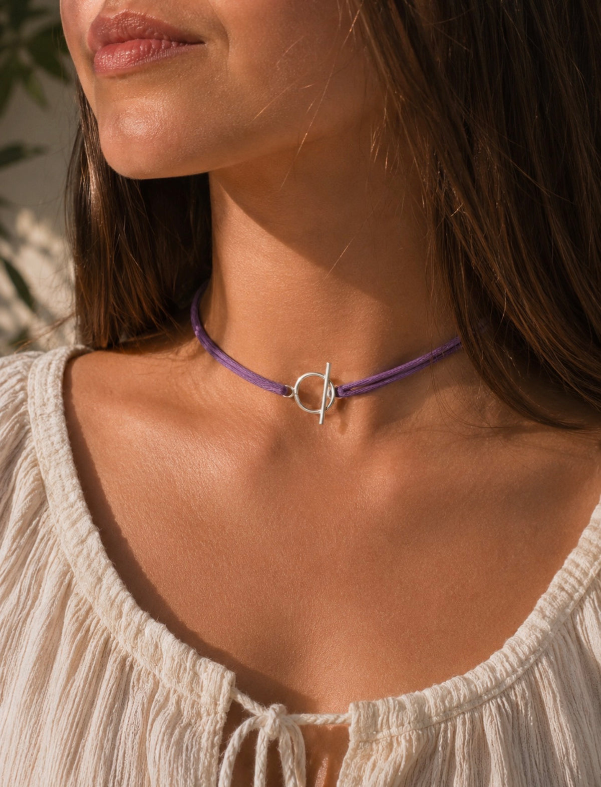 Collier Julia violet en cordon tressé porté en ras-de-cou par une femme en blouse blanche